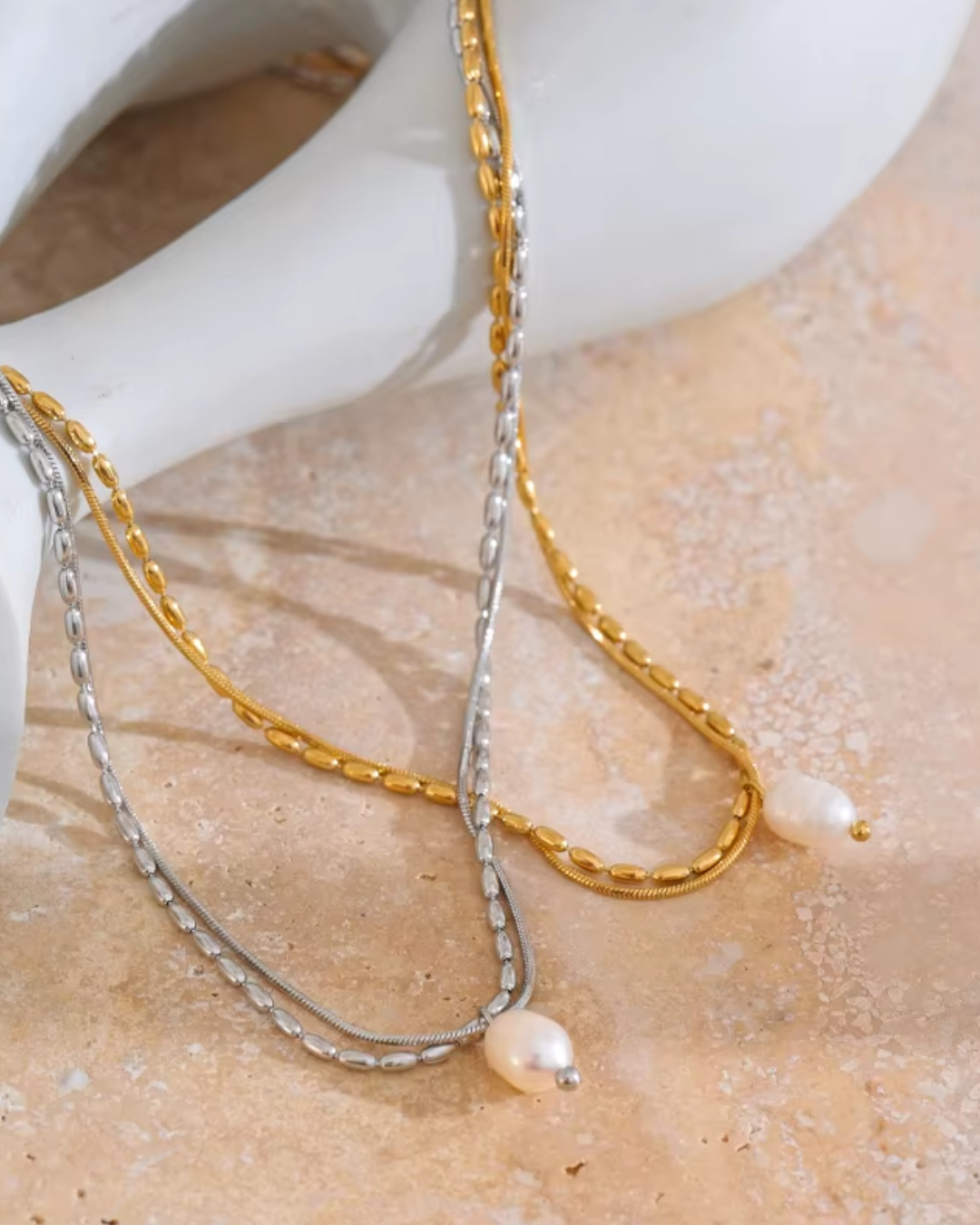 A silver and gold double-layered stainless steel necklace featuring a natural pearl pendant, designed for timeless elegance with a tarnish-resistant finish. Perfect for everyday sophistication. 